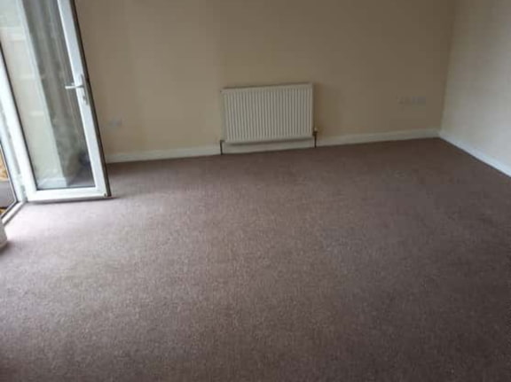 This is a photo of a living room after it has been cleaned. The room is empty and has a brown carpet that has been steam cleaned works carried out by Mill Hill Carpet Cleaning.